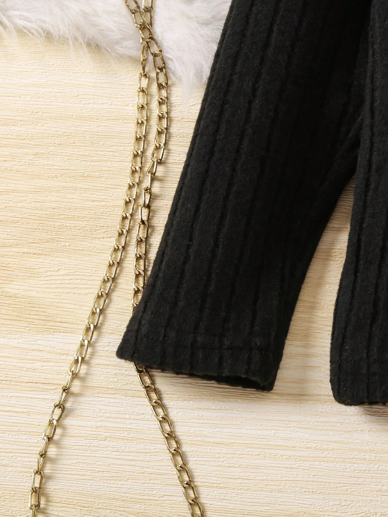 Black ribbed sweater sleeve with gold chain on a textured beige surface