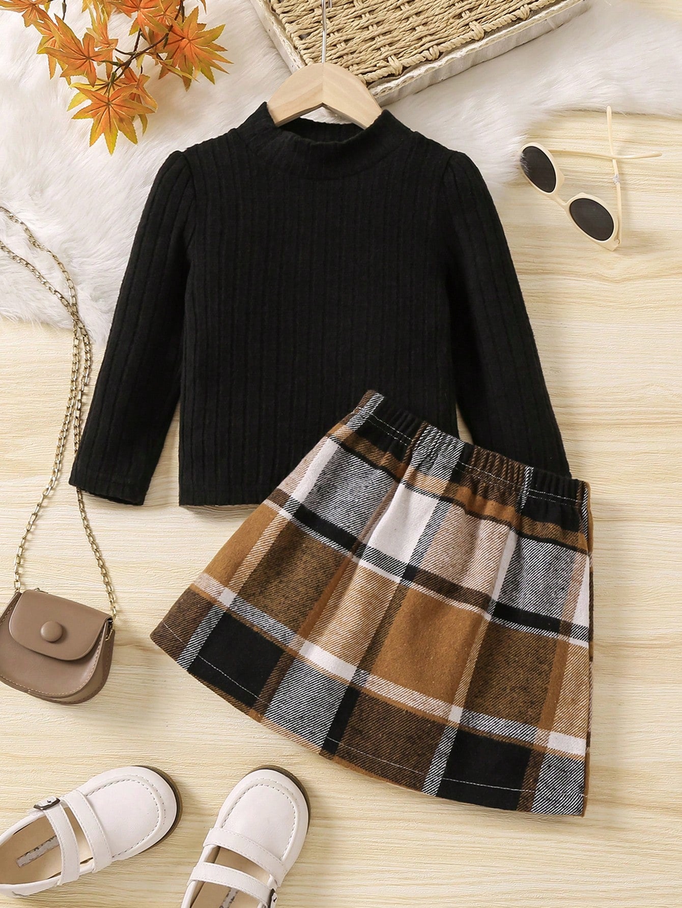 Black turtleneck and plaid skirt set on a wooden surface with shoes and a handbag.