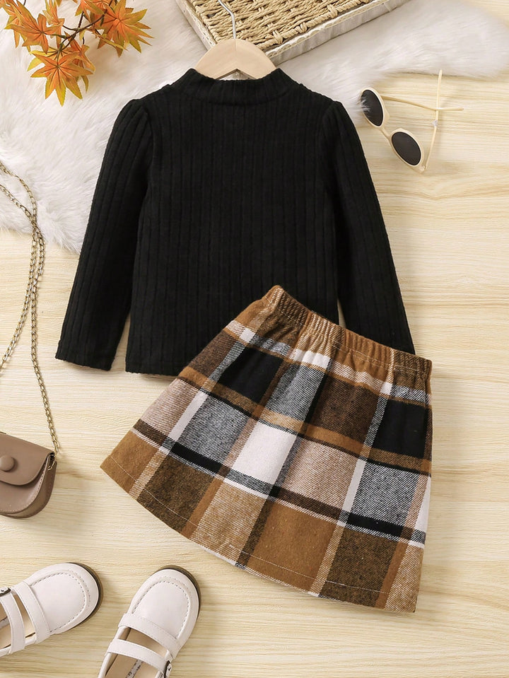 Black sweater and plaid skirt set on a wooden surface with accessories.