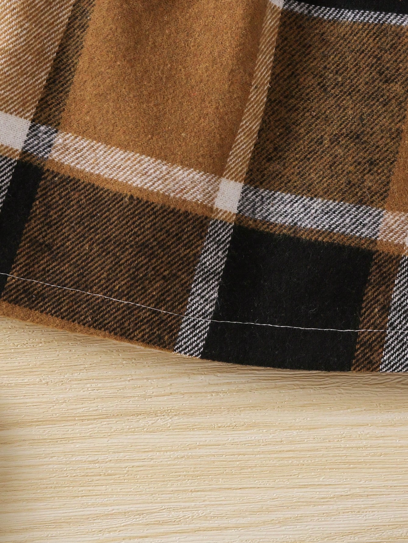 Close-up of plaid fabric with brown, black, and beige colors on a wooden surface.