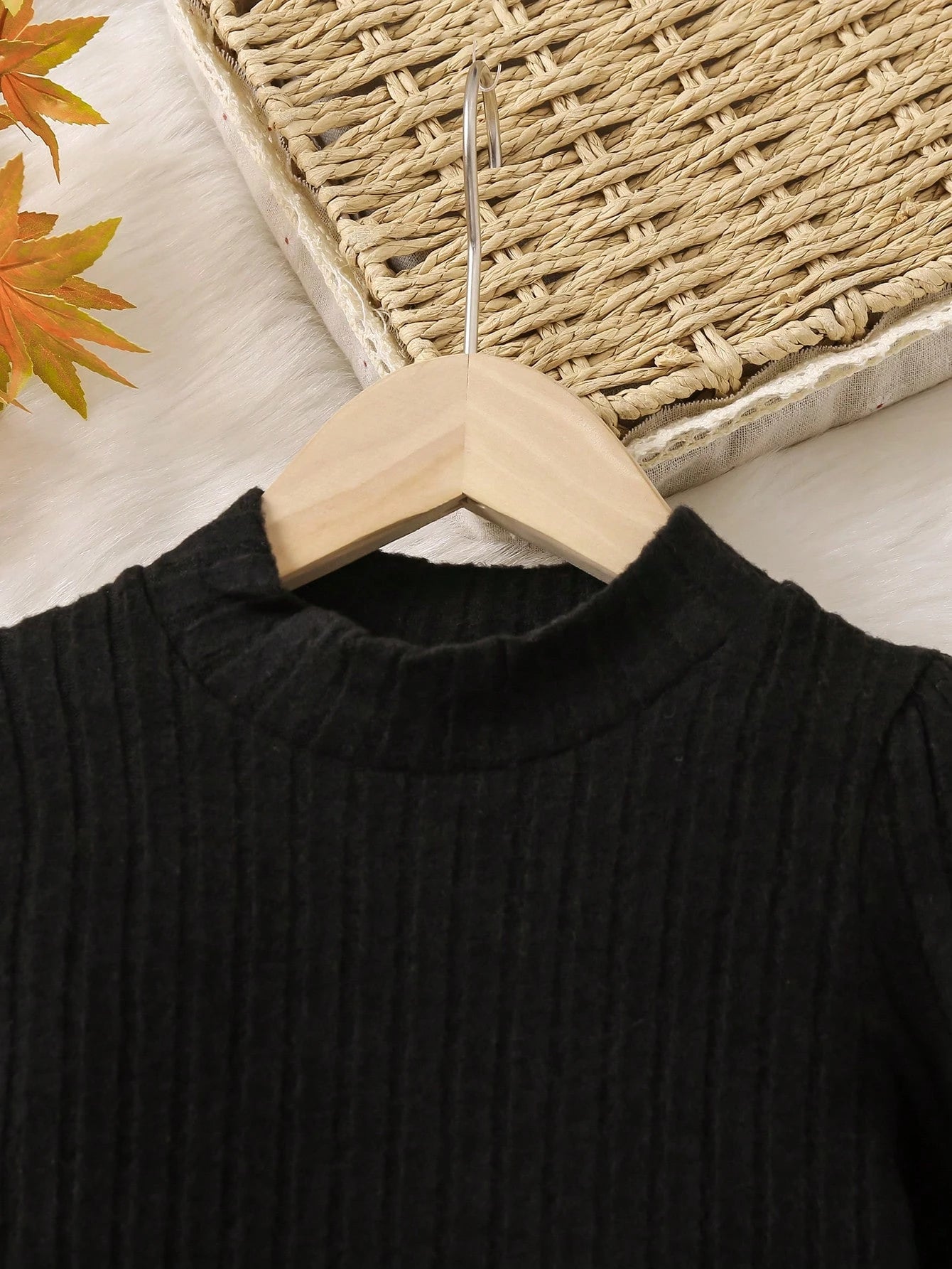 Black sweater on a wooden hanger with a woven basket and autumn leaves in the background