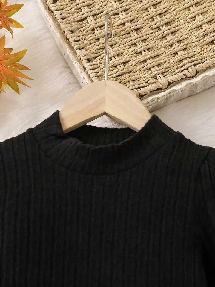 Black sweater on a wooden hanger with a woven basket and autumn leaves in the background