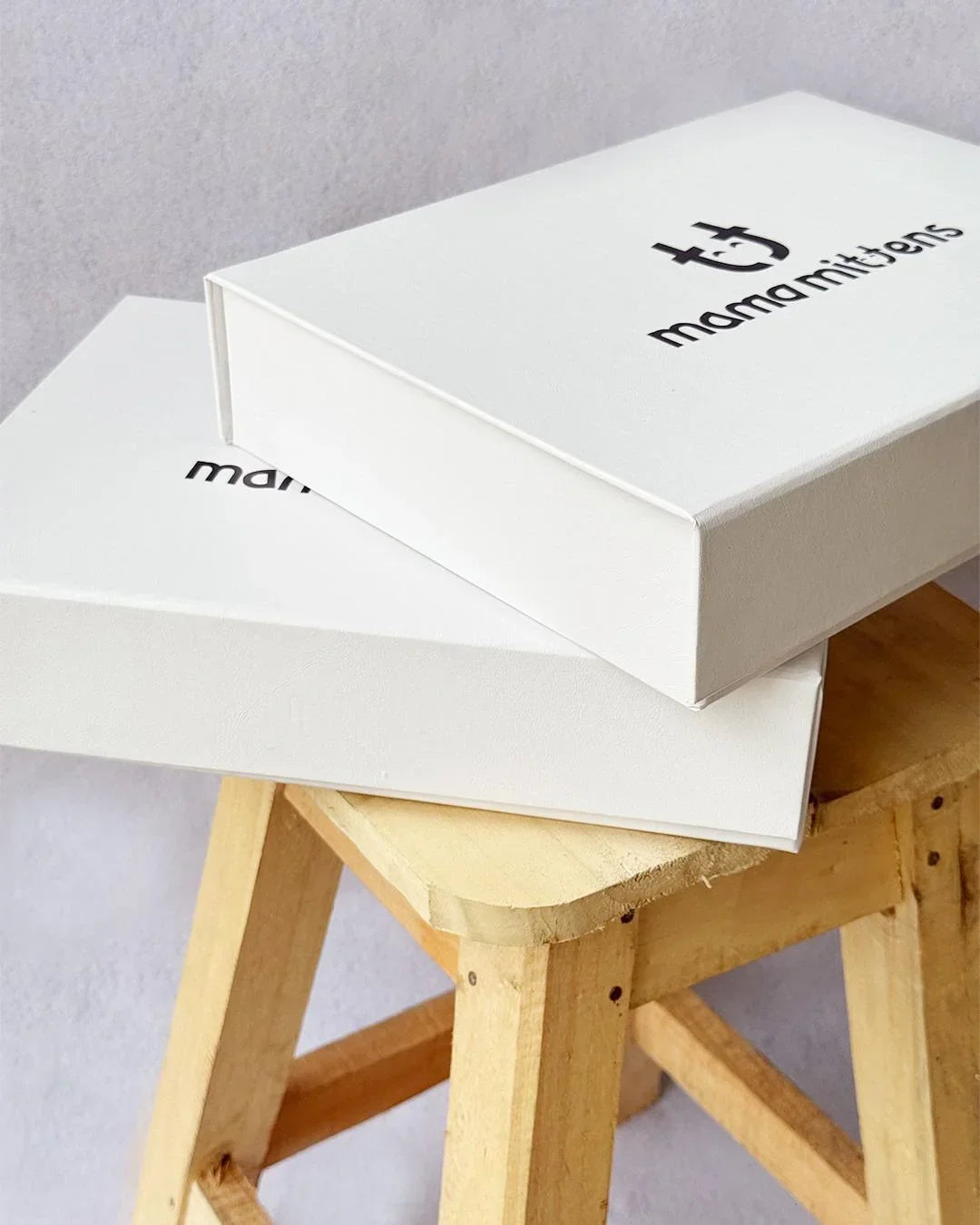 Two white boxes with 'mamalinters' branding on a wooden stool against a gray background