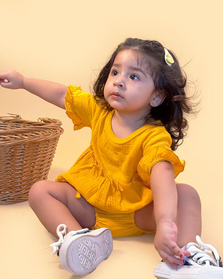 Child in a yellow outfit sitting on the floor with a beige background