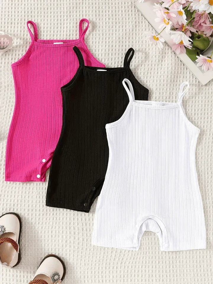 Three ribbed tank rompers in pink, black, and white on a textured surface with flowers and sandals.