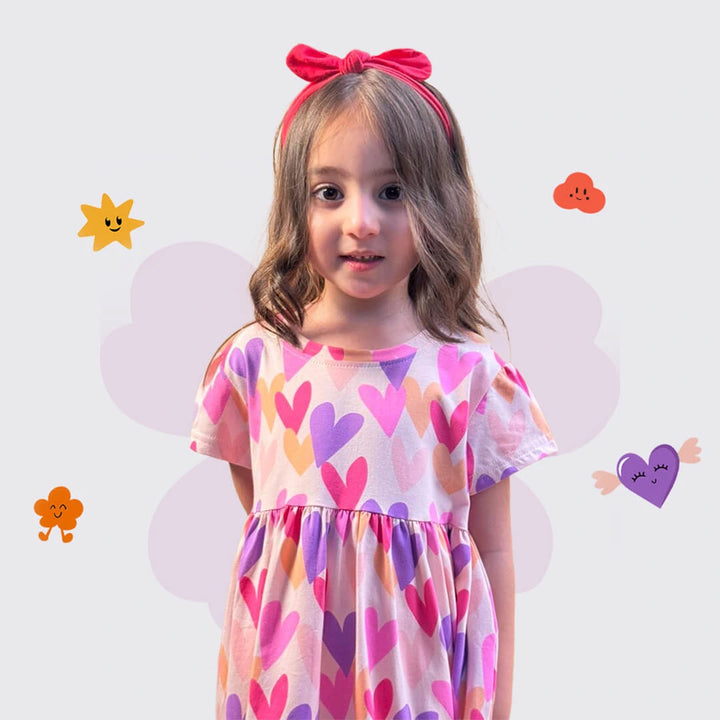 Young girl wearing a dress with heart pattern and a red bow, against a light purple background with cartoonish decorations.