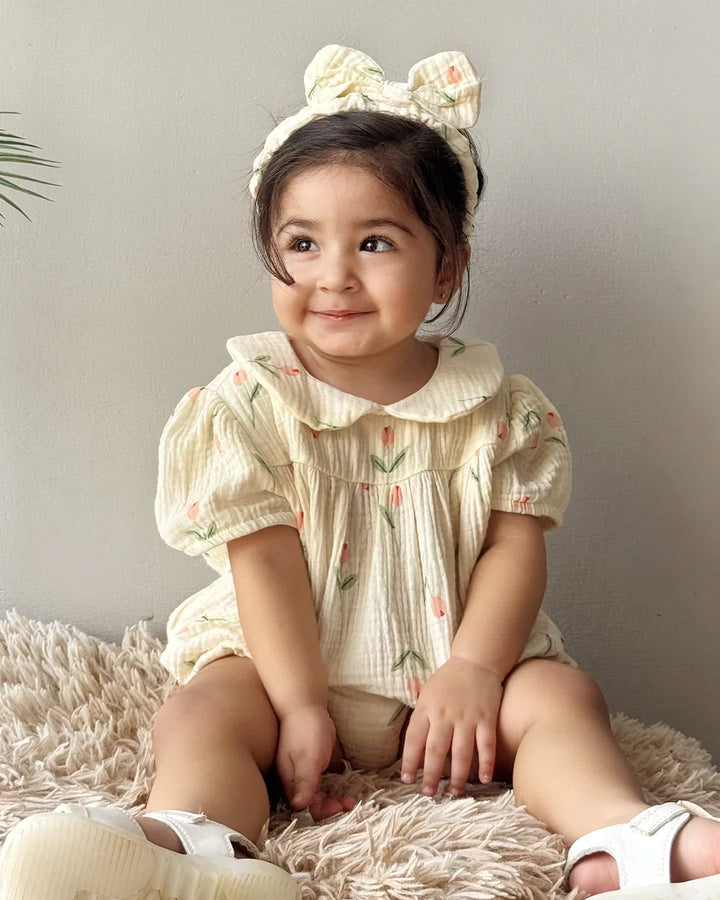 Child wearing a floral headband and a light-colored dress sitting on a fluffy surface.