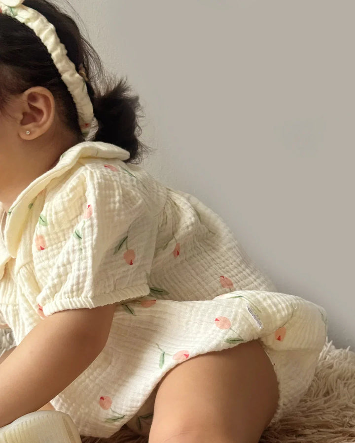 Child wearing a white outfit with pink floral patterns on a plain background