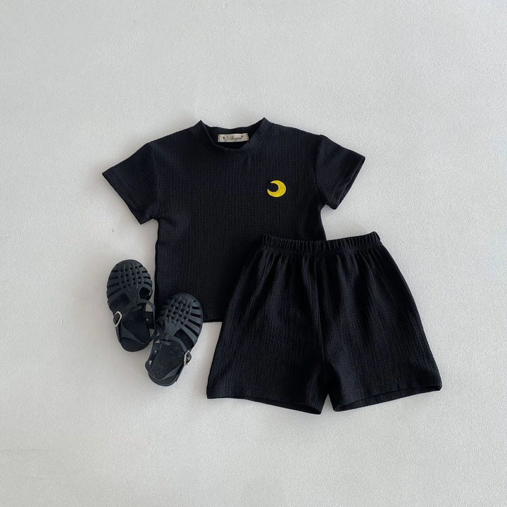 Black t-shirt with yellow design and black shorts on a light gray background