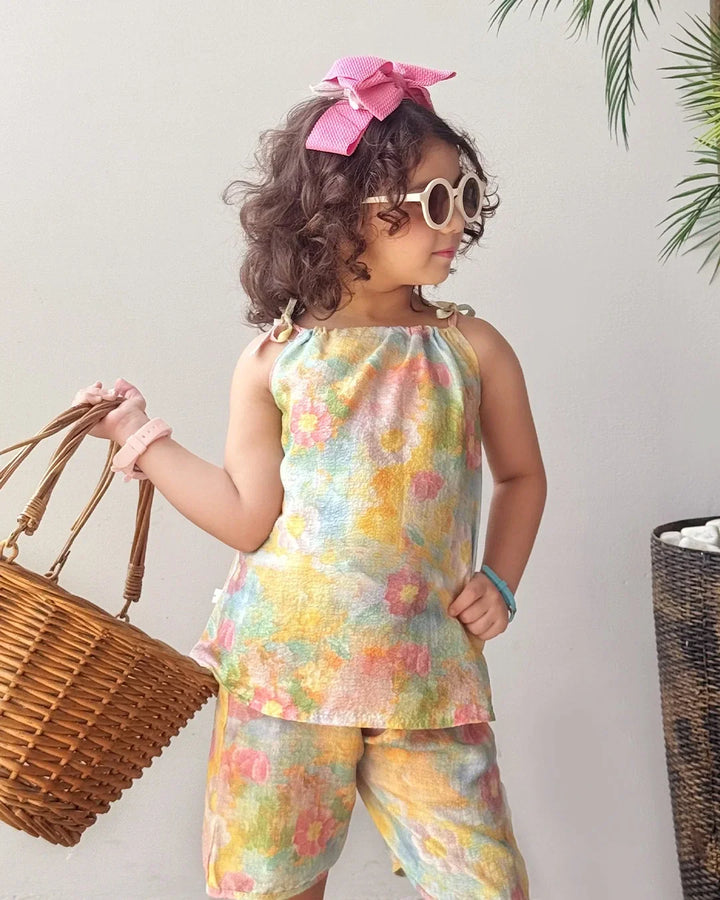 Child wearing a colorful floral outfit with a pink bow and sunglasses, holding a woven bag.