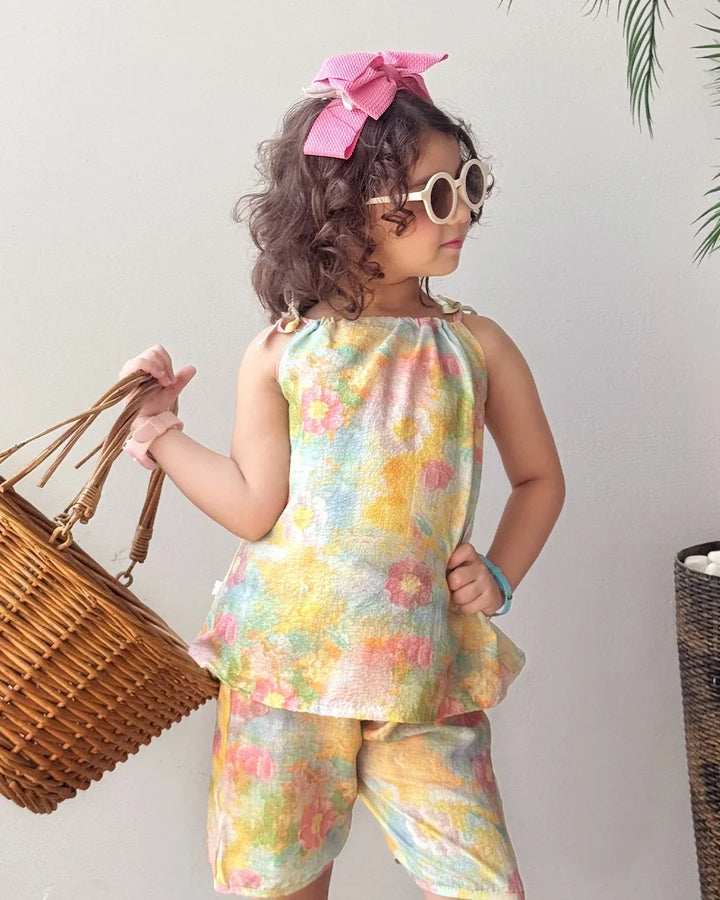 Child wearing a colorful floral outfit with a pink bow and sunglasses, holding a wicker basket.