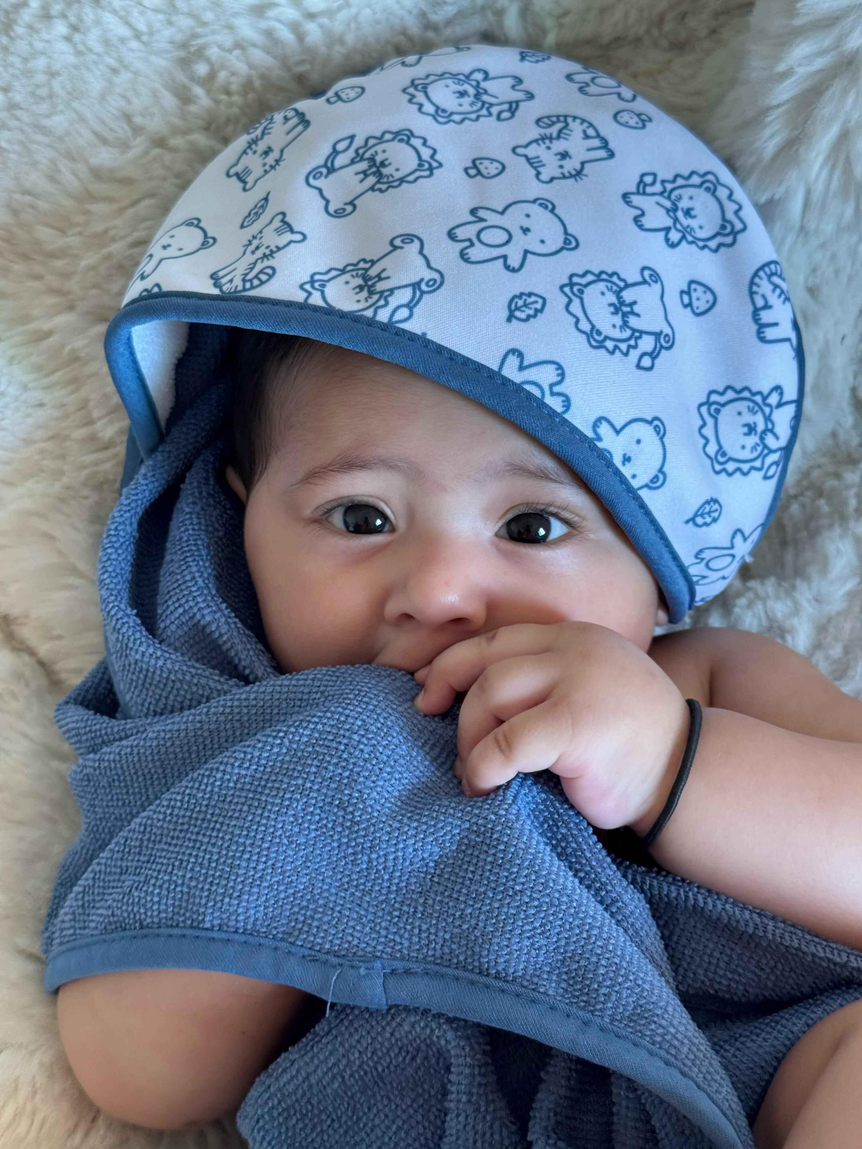 Baby wrapped in a blue towel with a patterned cap, lying on a soft surface.