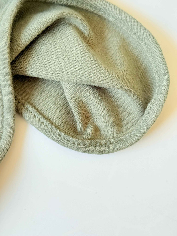 Close-up of a sage green baby blanket corner showing soft cotton fabric texture and neatly stitched rounded edges.