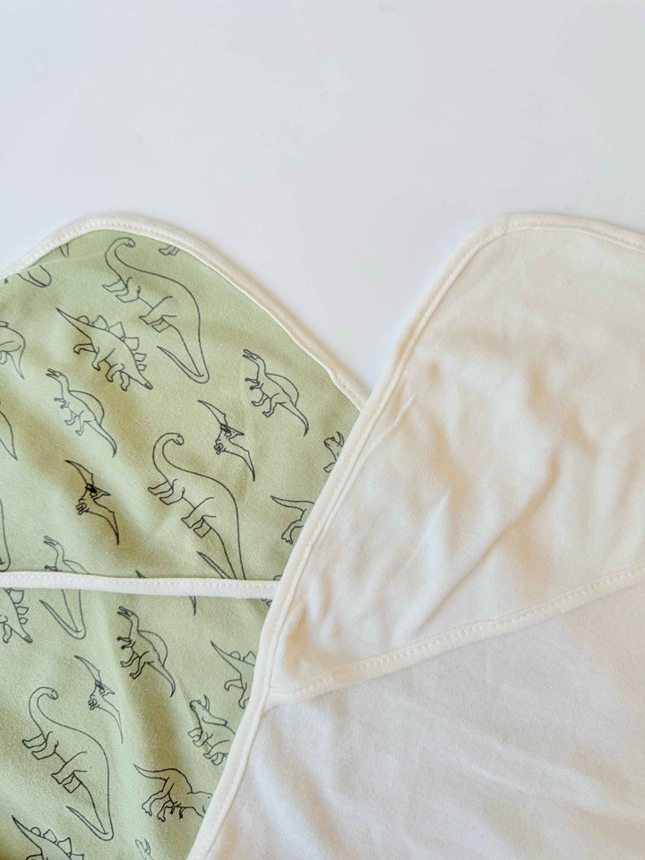 Two hooded wrapping sheets with dinosaur print in olive green and white colors, showing the fabric texture and design.