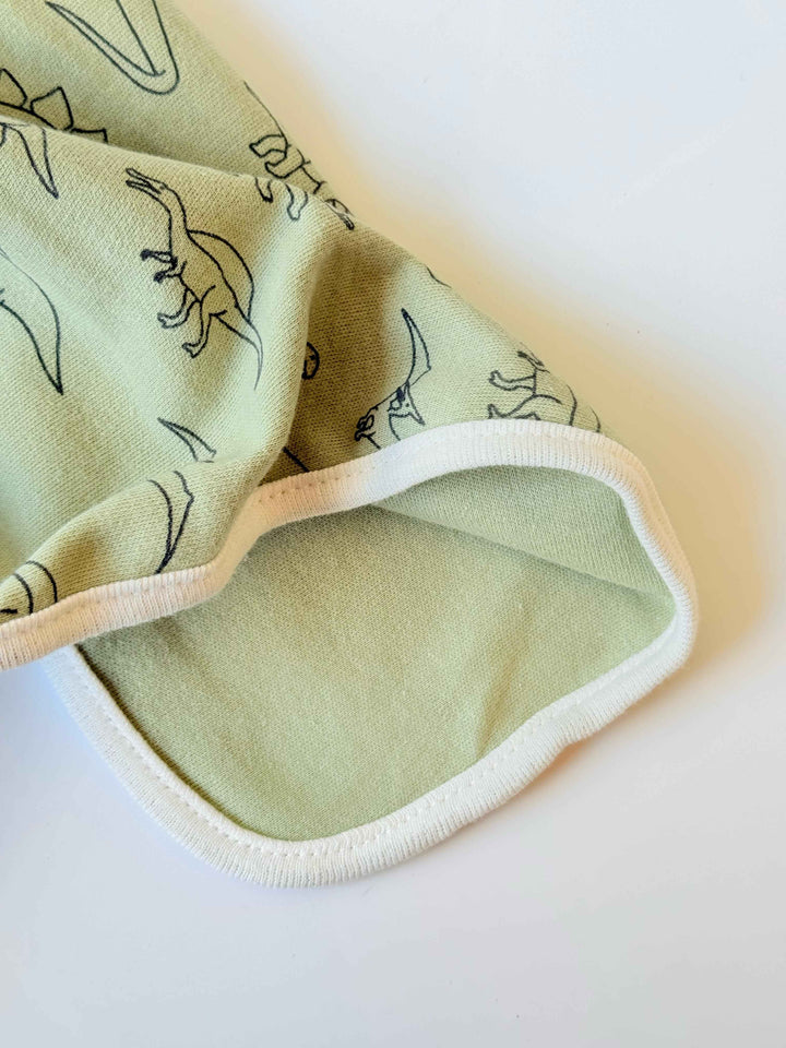 Close-up of a sage green baby blanket corner showing soft cotton fabric texture and neatly stitched rounded edges.