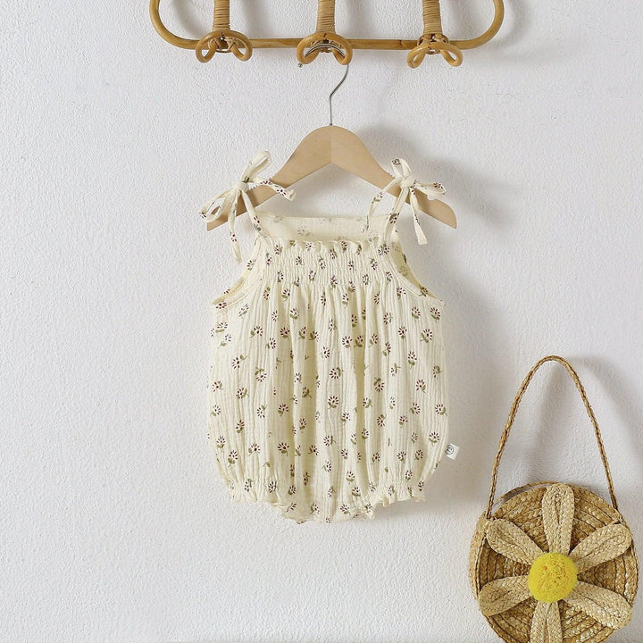 Baby romper with floral pattern hanging on a hook next to a small wicker bag with a flower design.