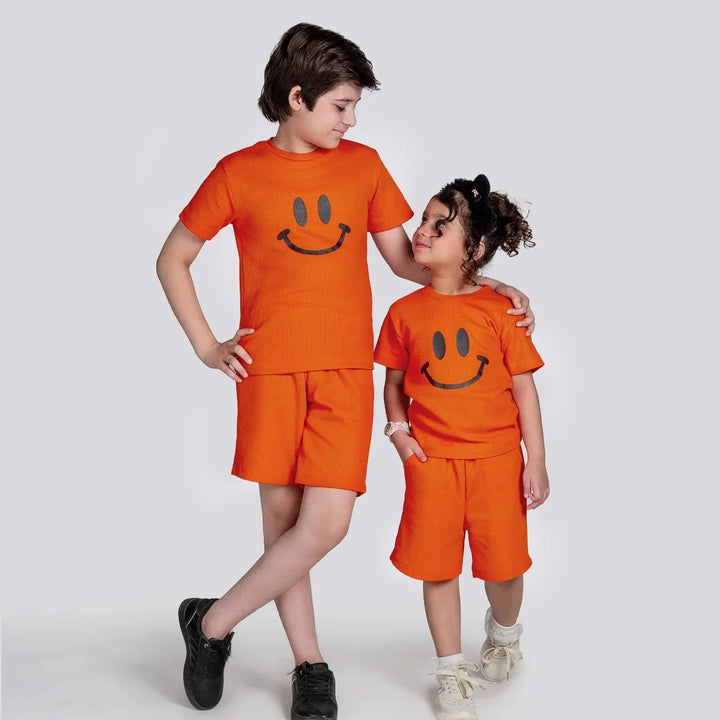 Two children wearing matching orange outfits with smiley face designs on a white background