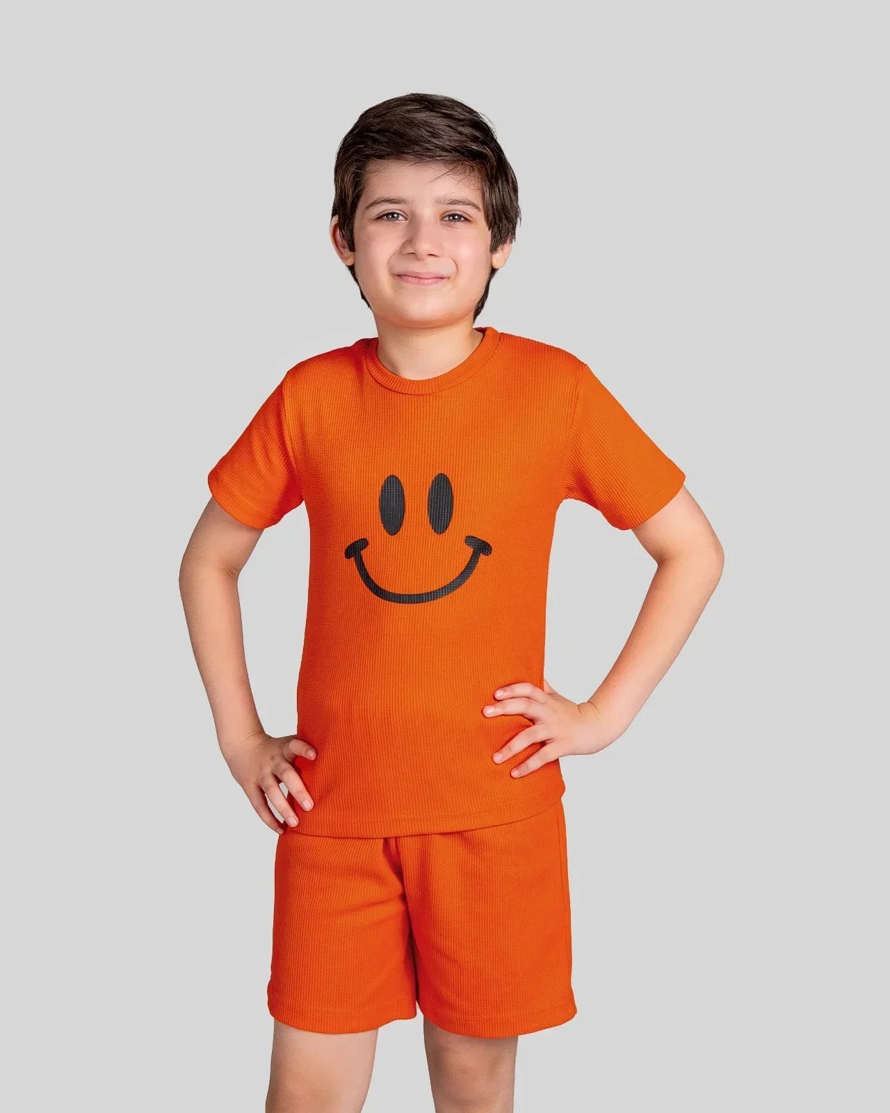 Child wearing an orange outfit with a smiley face design on a plain background