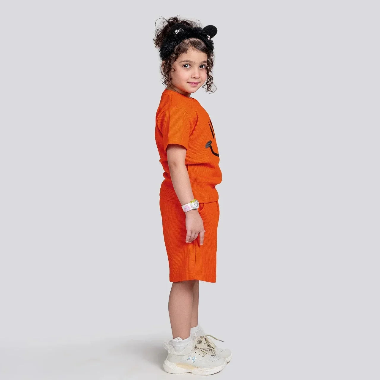 Child wearing an orange outfit with a black logo on a light gray background