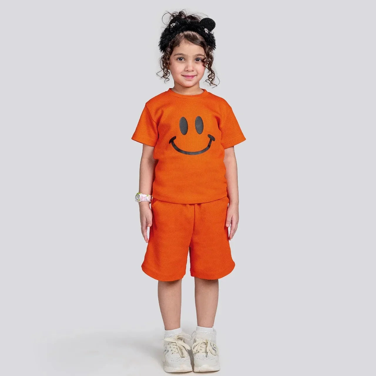 Child wearing an orange outfit with a smiley face design on a plain background