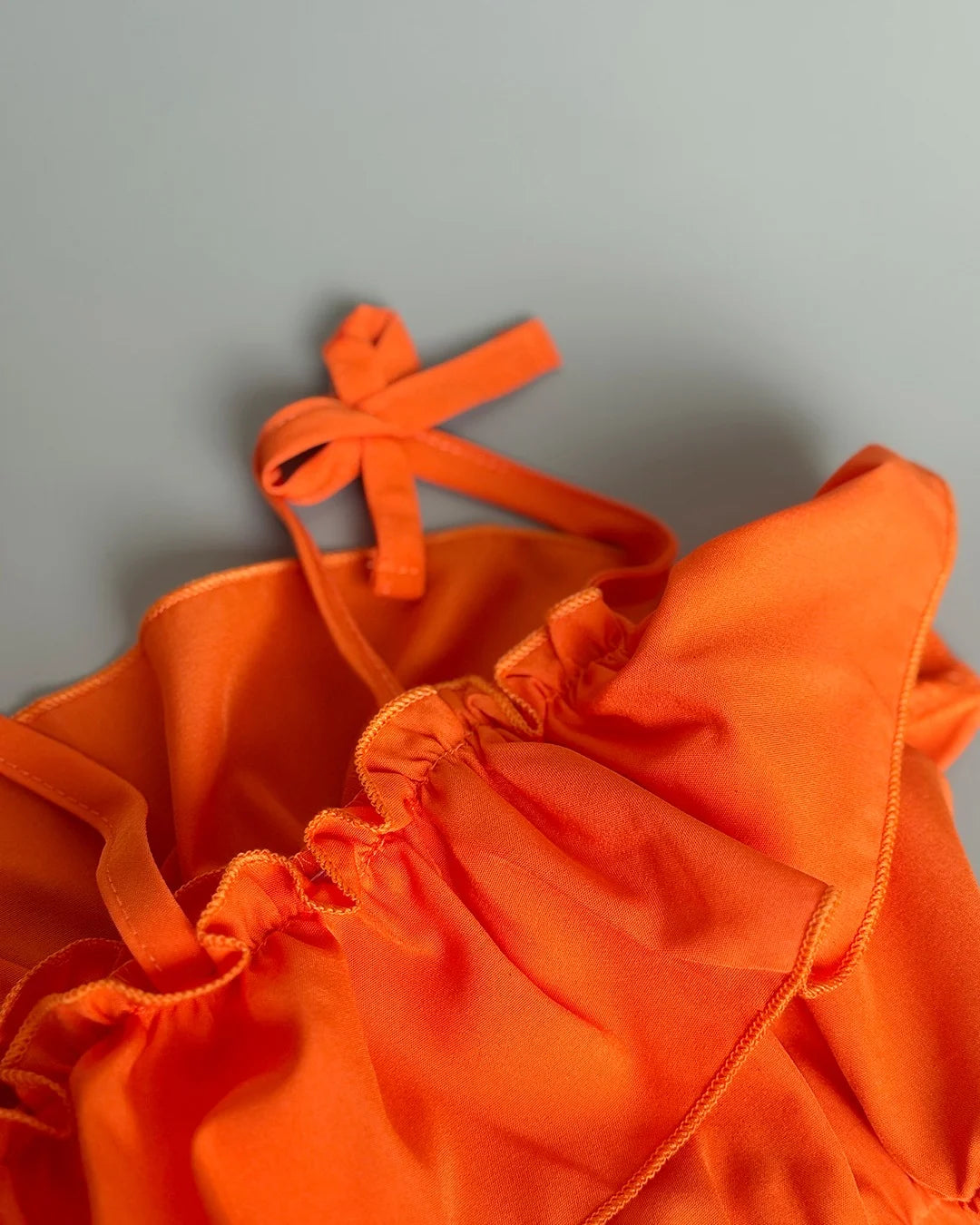 Orange bikini top with ruffled details on a gray background