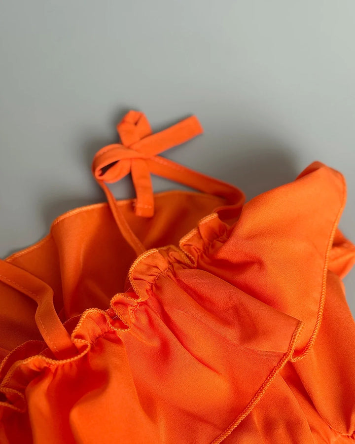 Orange bikini top with ruffled details on a gray background