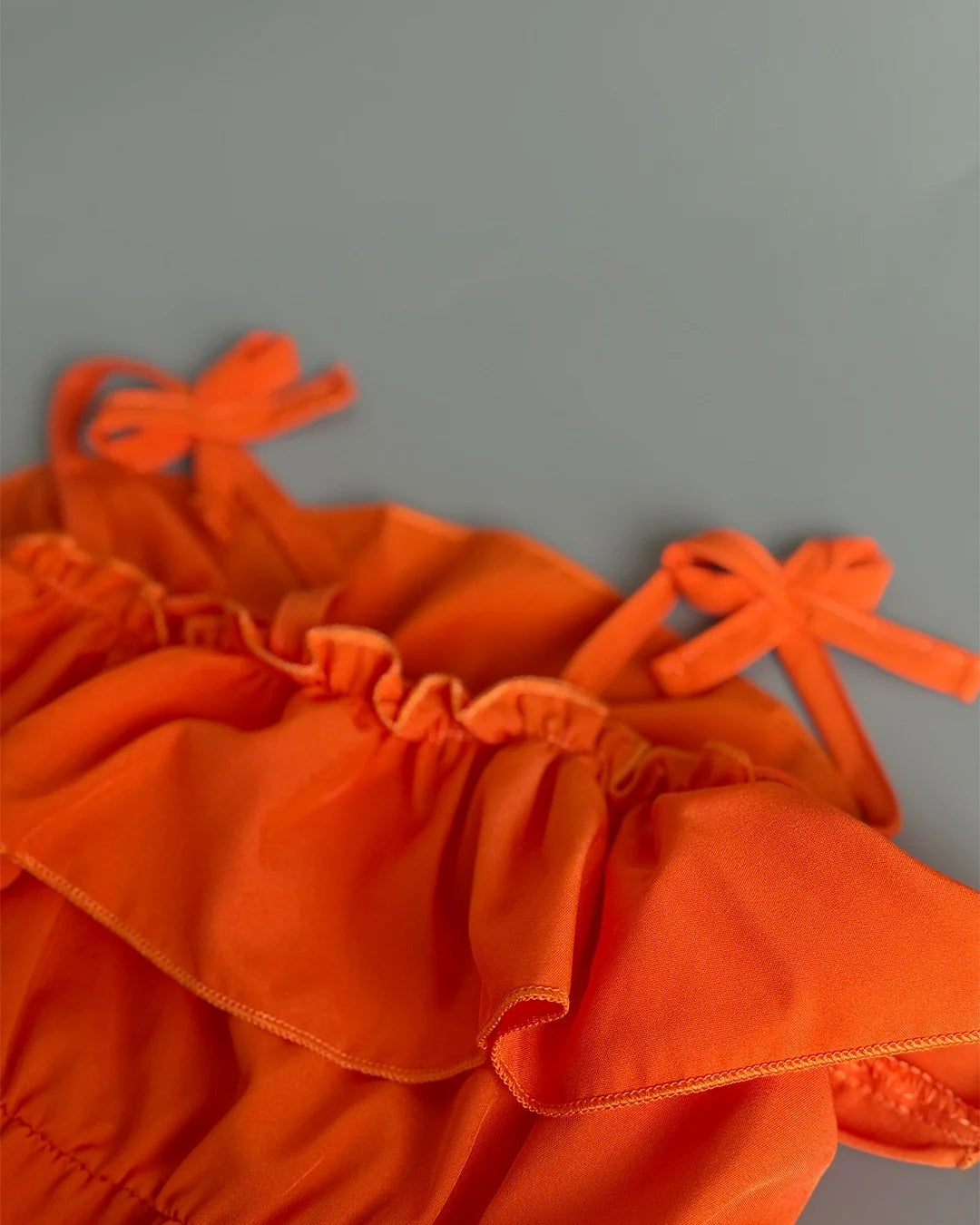 Orange fabric with ruffled edges and tied straps on a gray background