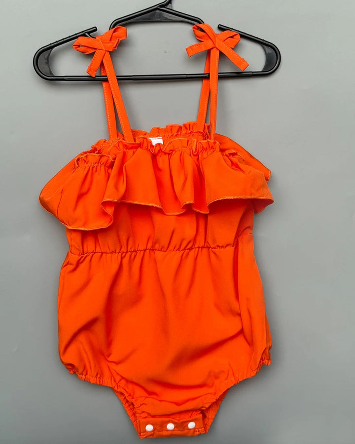Orange romper with ruffled details on a gray background