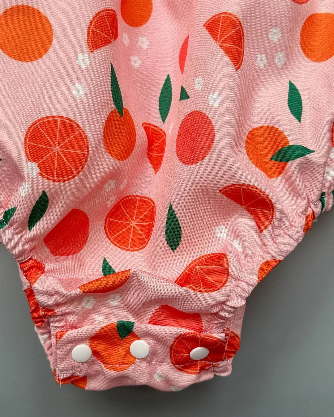 Pink baby bloomers with orange fruit pattern on a gray background
