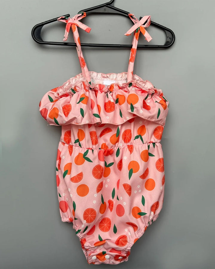 Pink baby romper with fruit pattern on a hanger against a gray background