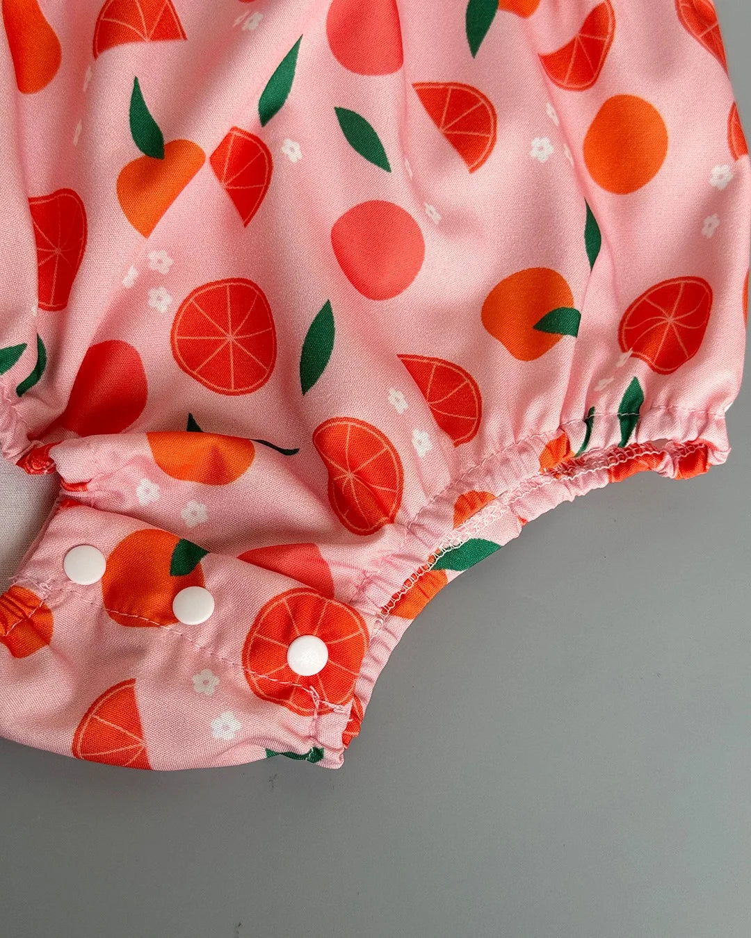 Pink baby bloomers with orange and green fruit pattern on a gray background