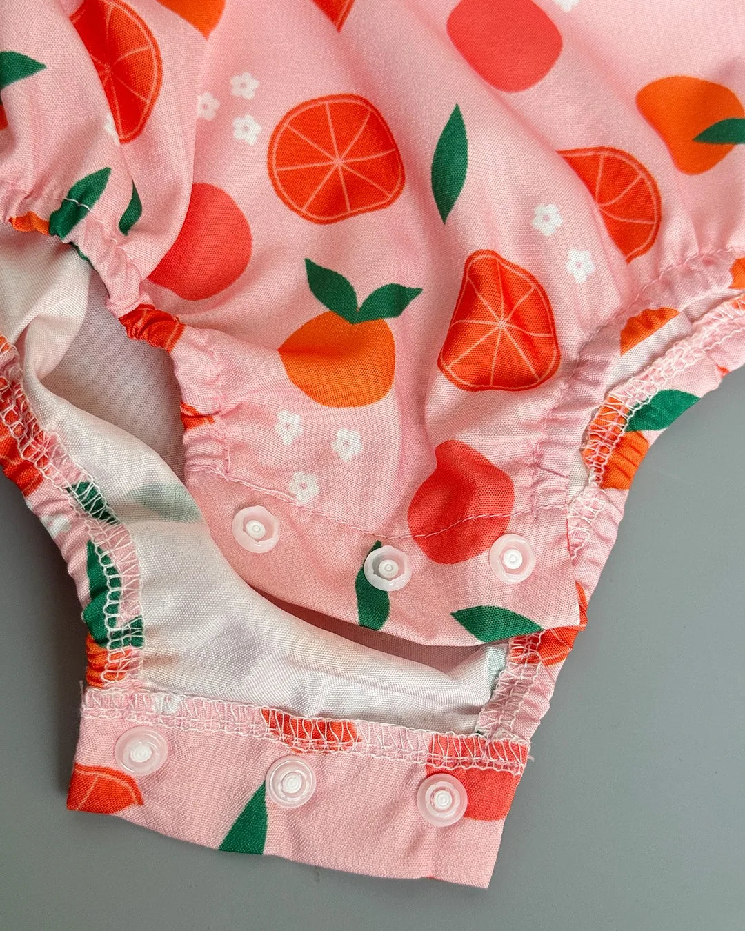 Pink baby bloomers with orange and green fruit pattern on a gray background