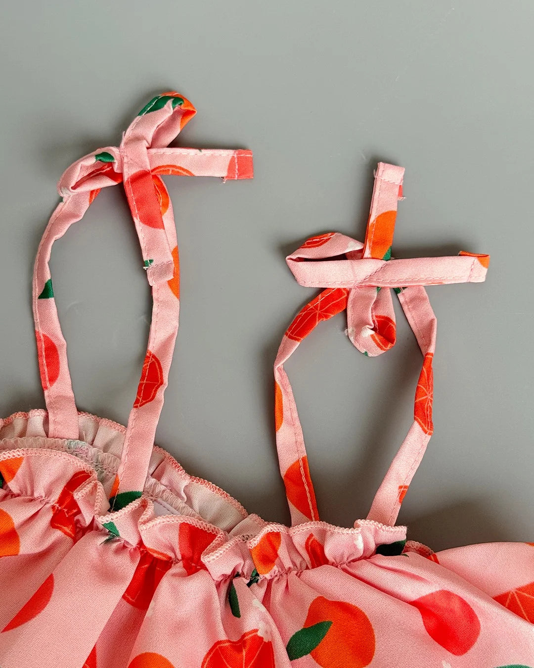 Pink dress with red apple pattern on straps against a gray background
