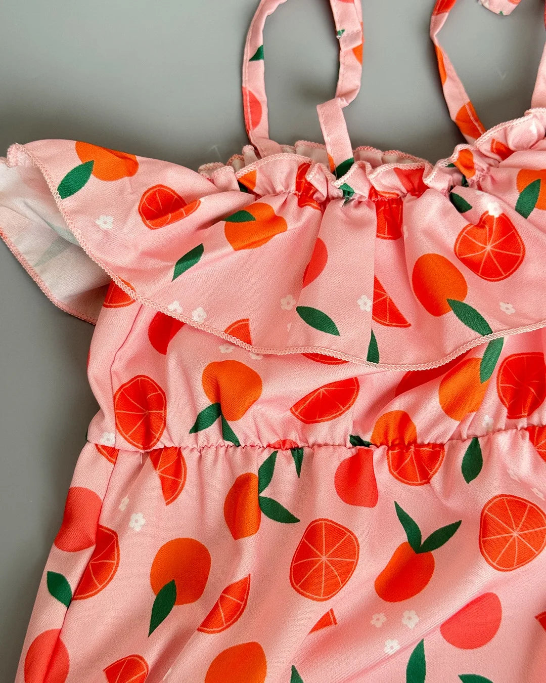 Pink children's dress with orange and green pattern on a gray background