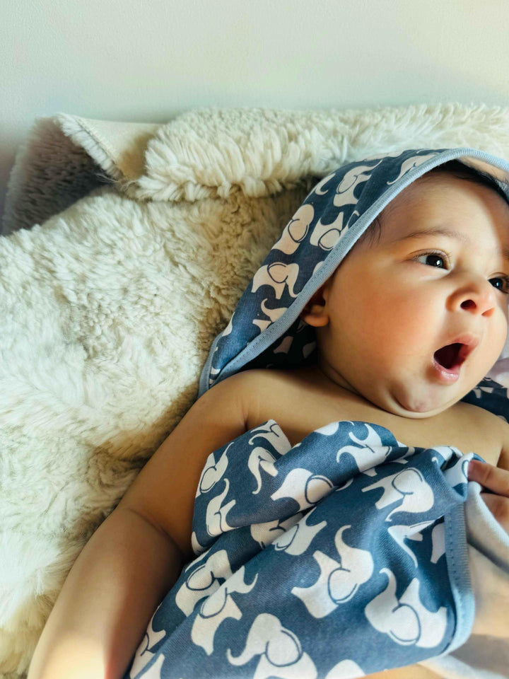 Baby wrapped in a blue towel with elephant patterns on a soft surface