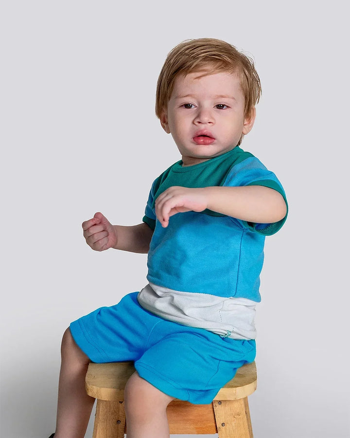 Child wearing a blue outfit sitting on a wooden stool against a plain background