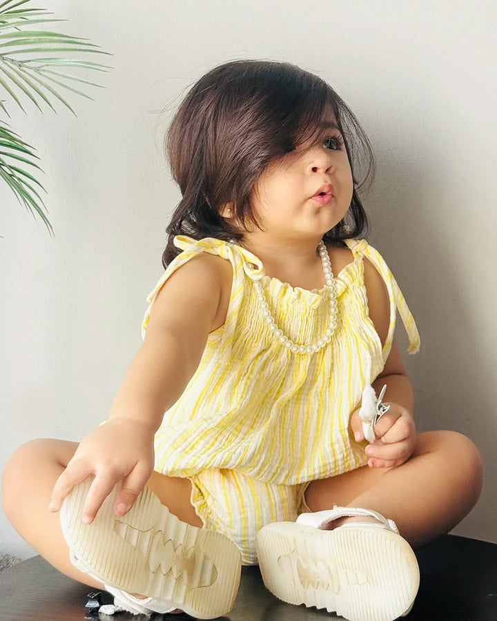 Child wearing a yellow outfit with ruffled top and shorts, sitting on a surface.