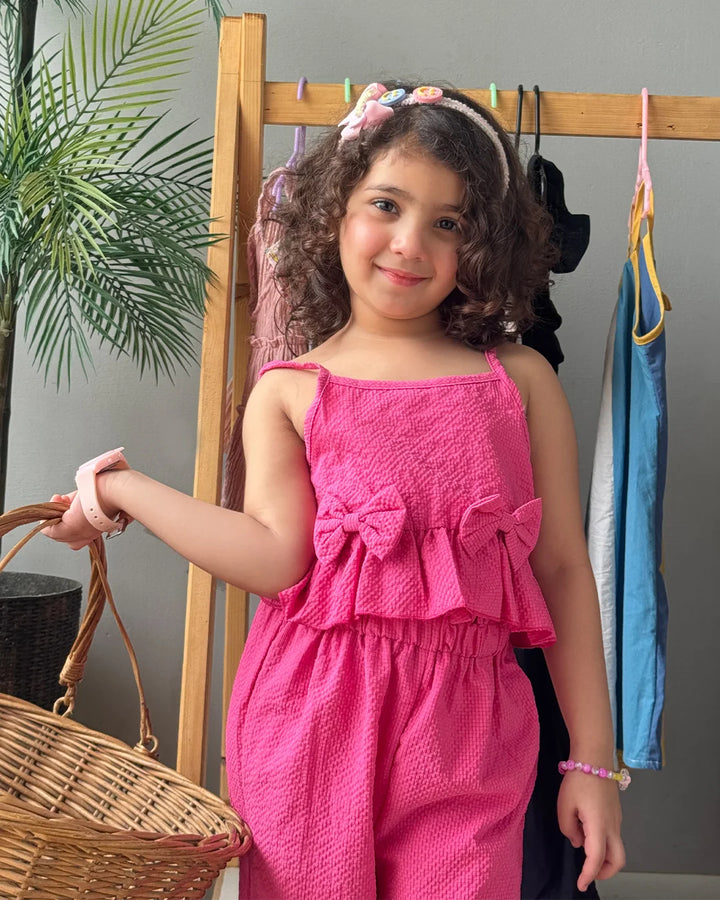 Young girl in a pink outfit standing next to a wooden rack with clothes.