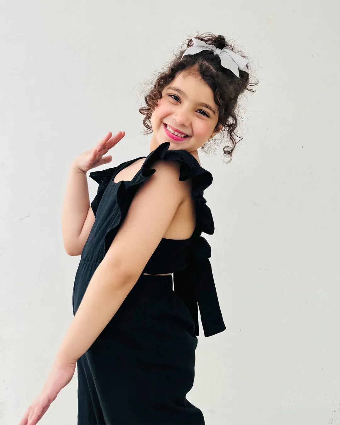 Young girl wearing a black dress with ruffled shoulders against a plain background