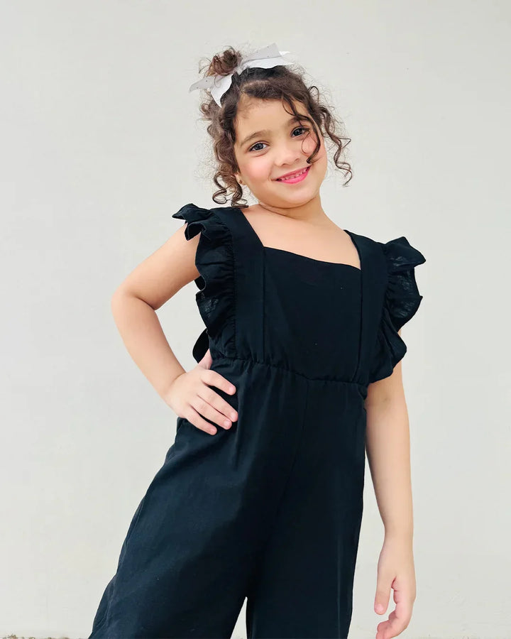 Young girl wearing a black ruffled jumpsuit against a plain background