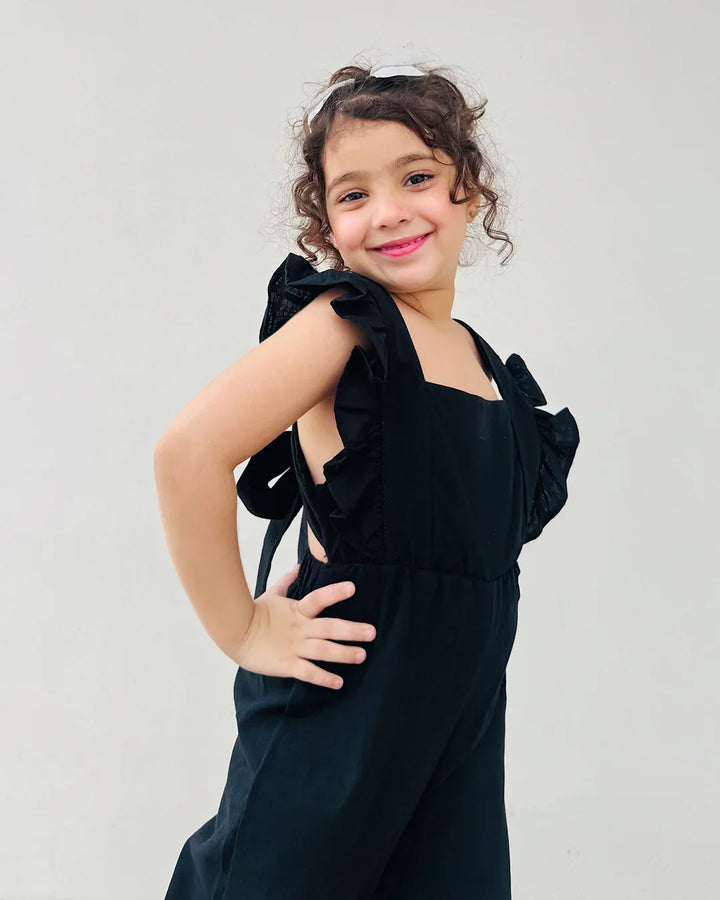 Young girl wearing a black dress with ruffled shoulders against a plain background