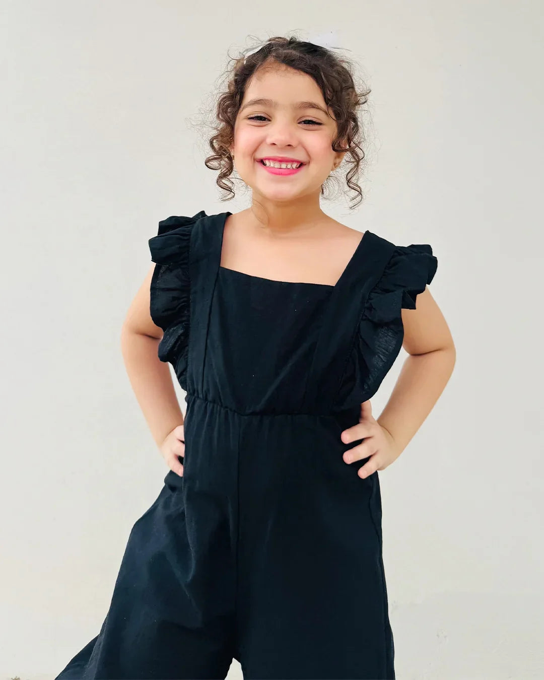 Young girl wearing a black ruffled jumpsuit against a plain background