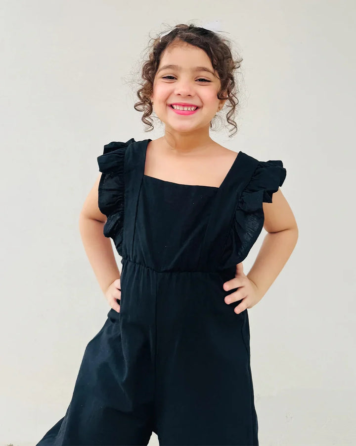 Young girl wearing a black ruffled jumpsuit against a plain background