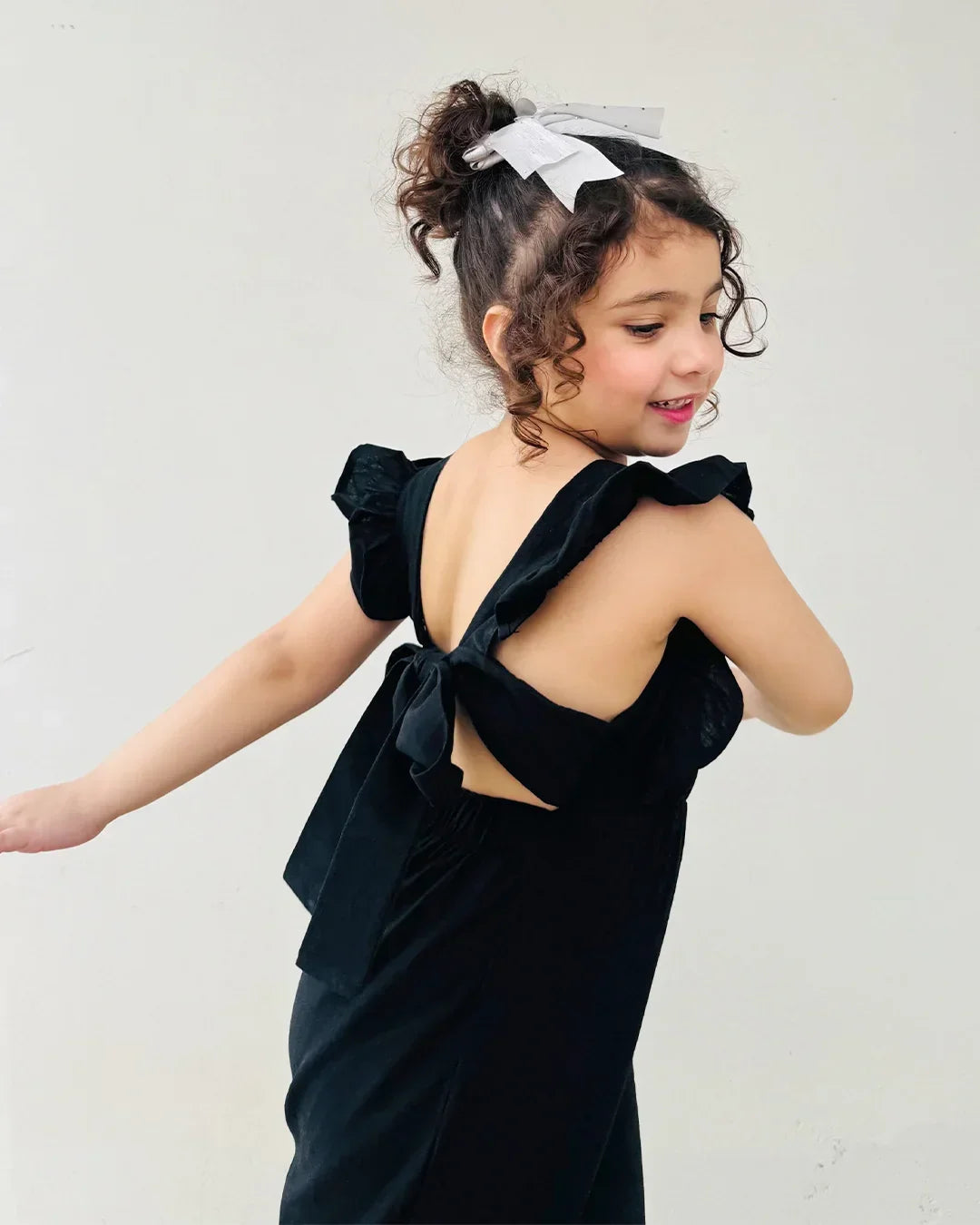 Young girl wearing a black dress with bow details on a plain background