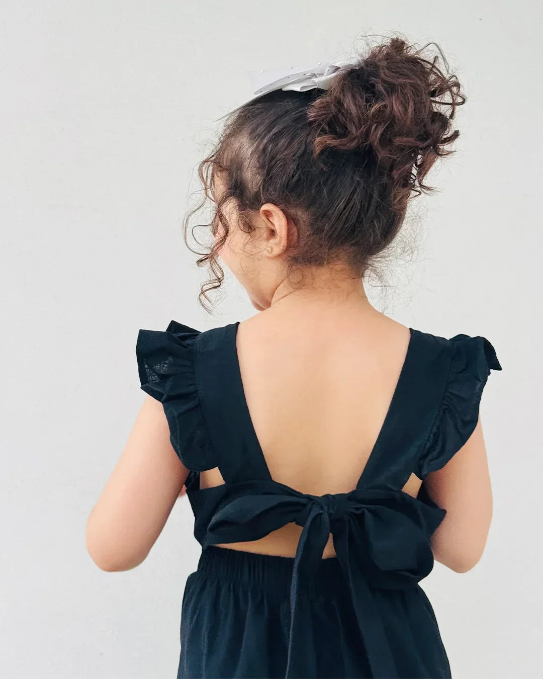 Child wearing a black dress with ruffled shoulders and a bow detail on a plain background