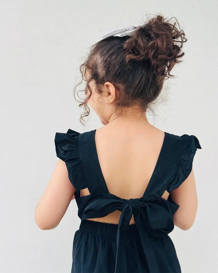 Child wearing a black dress with ruffled shoulders and a bow detail on a plain background
