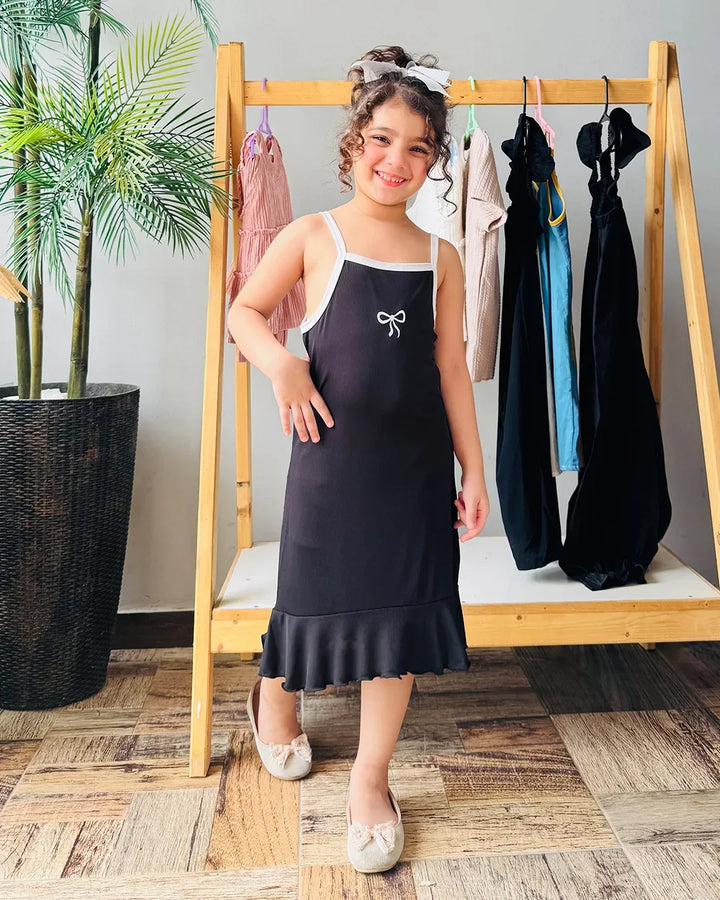 Young girl in a black dress standing in front of a wooden rack with clothes.