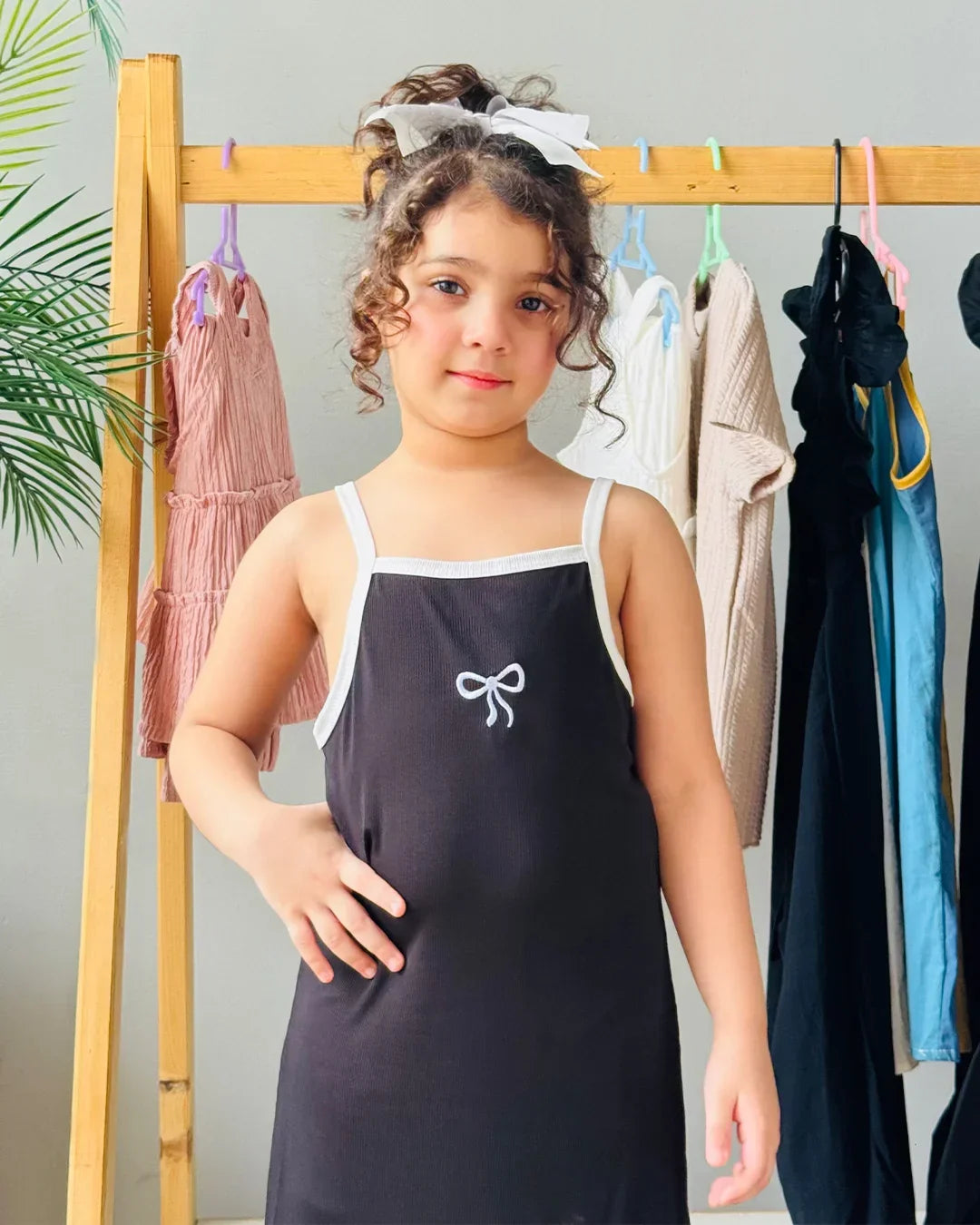 Young girl wearing a black apron with a white bow design in front of a clothing rack.