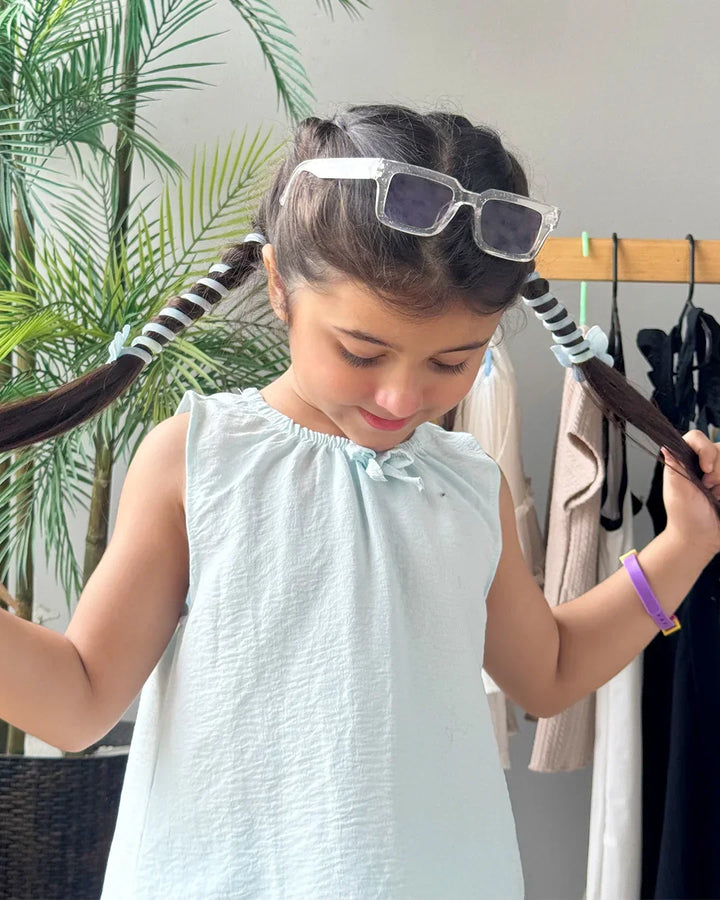 Young girl styling her hair with a hairbrush in a room with plants and clothing racks.