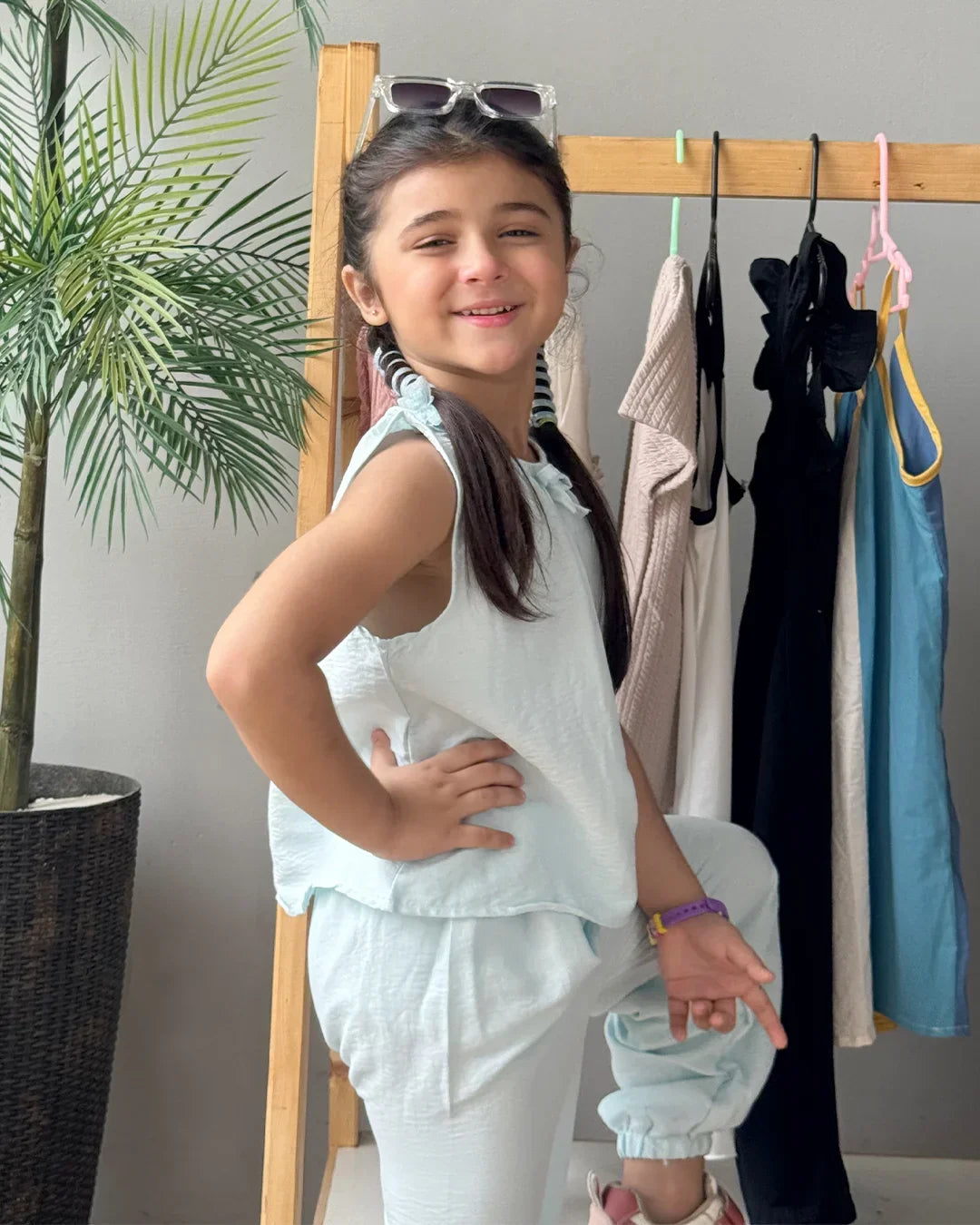 Young girl in light blue outfit standing in front of a clothing rack with clothes hanging on it.